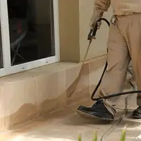 General pest control technician spraying exterior perimeter around a home in Albany, NY