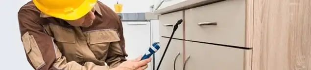 Roach exterminator applying treatment under kitchen cabinets in Albany, NY