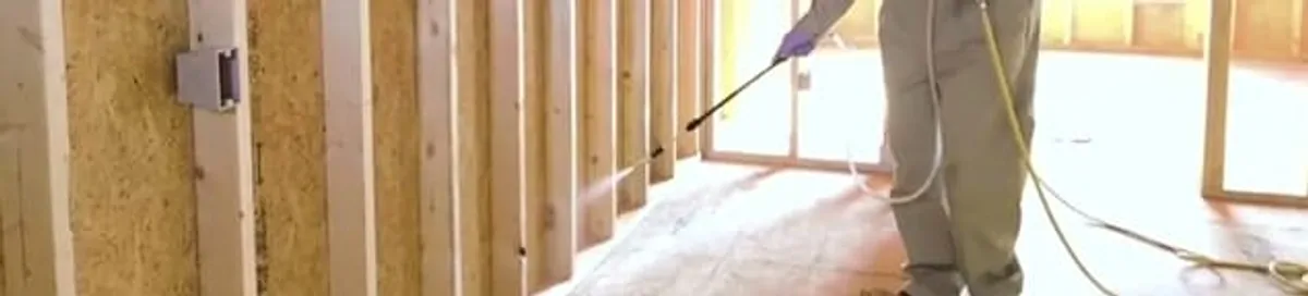 Termite treatment technician applying spray along framing and unfinished walls in Albany, NY
